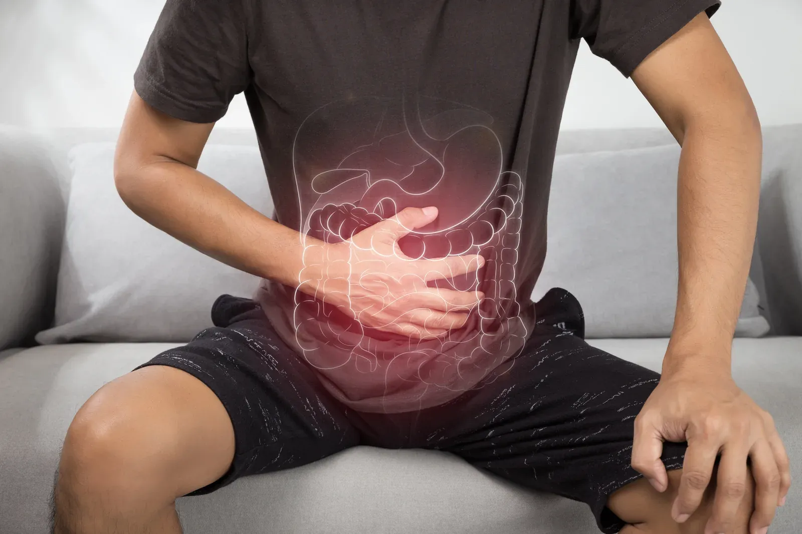 A man sitting hunched on a sofa, an illustration of the digestive tract glowing over his abdomen
