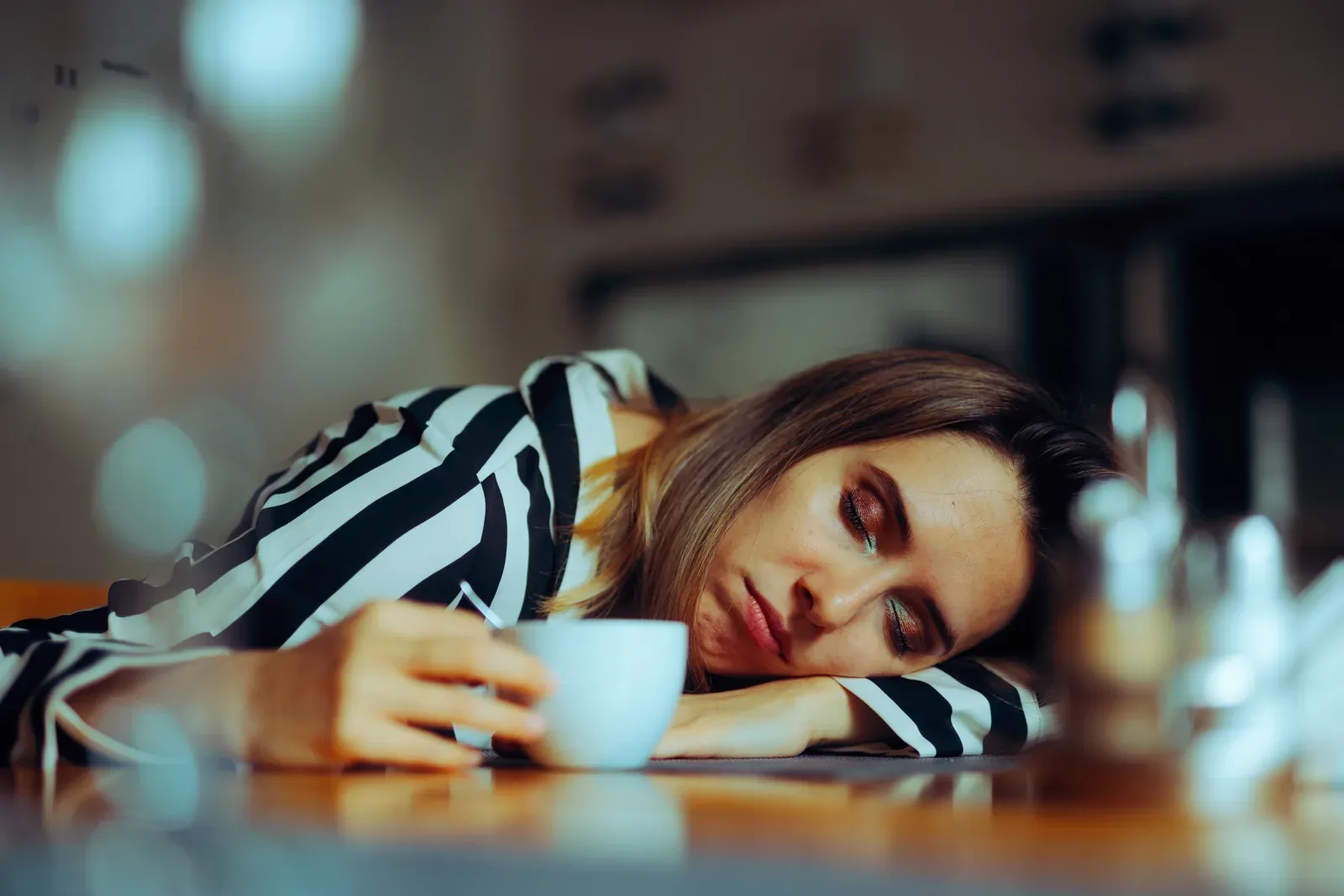 A woman resting her head on her arm at a cafe table beside a cup of coffee