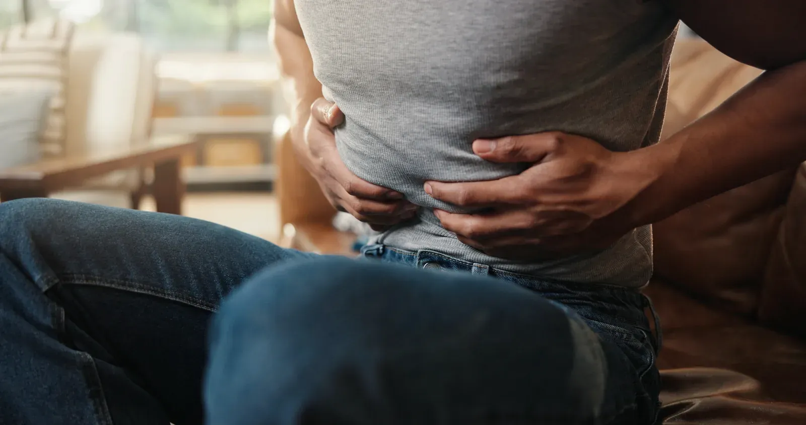 A man sitting forward with both hands pressed against his stomach