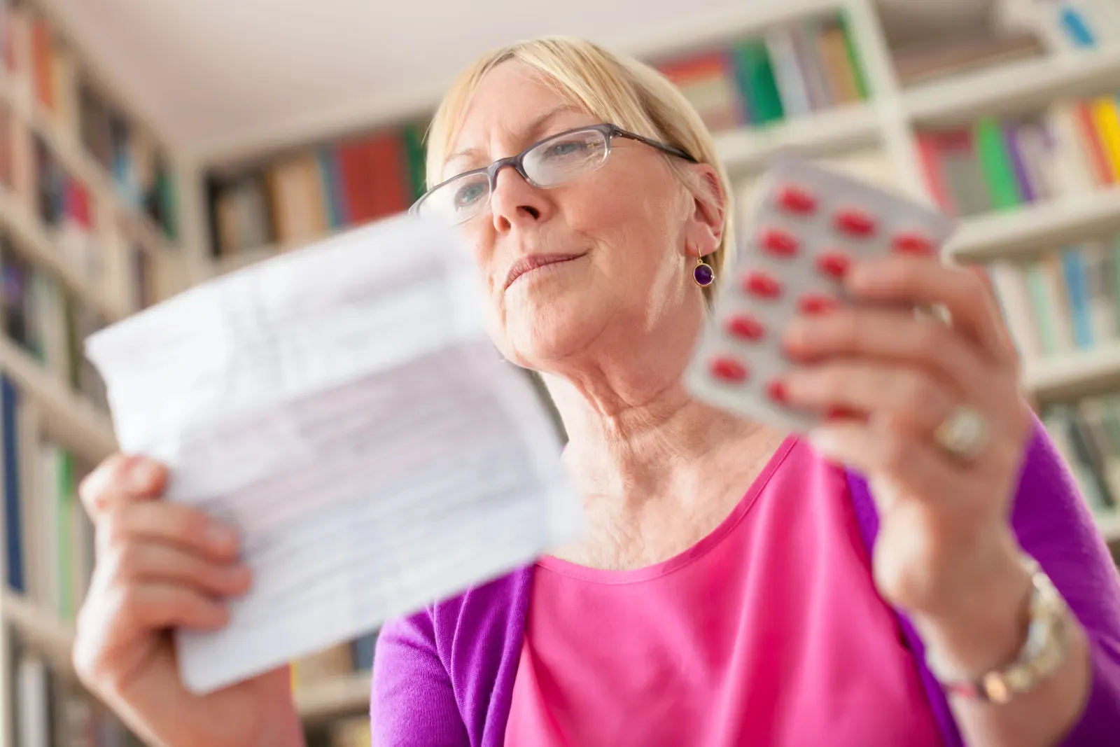 An older woman reading a prescription printout while holding a blister pack of tablets